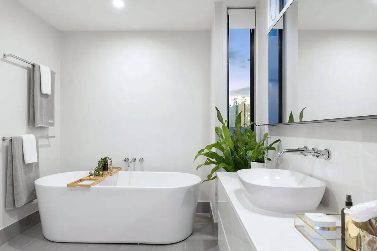 A white bathroom with a freestanding bath, a wall basin, towels on a rail and a large plant