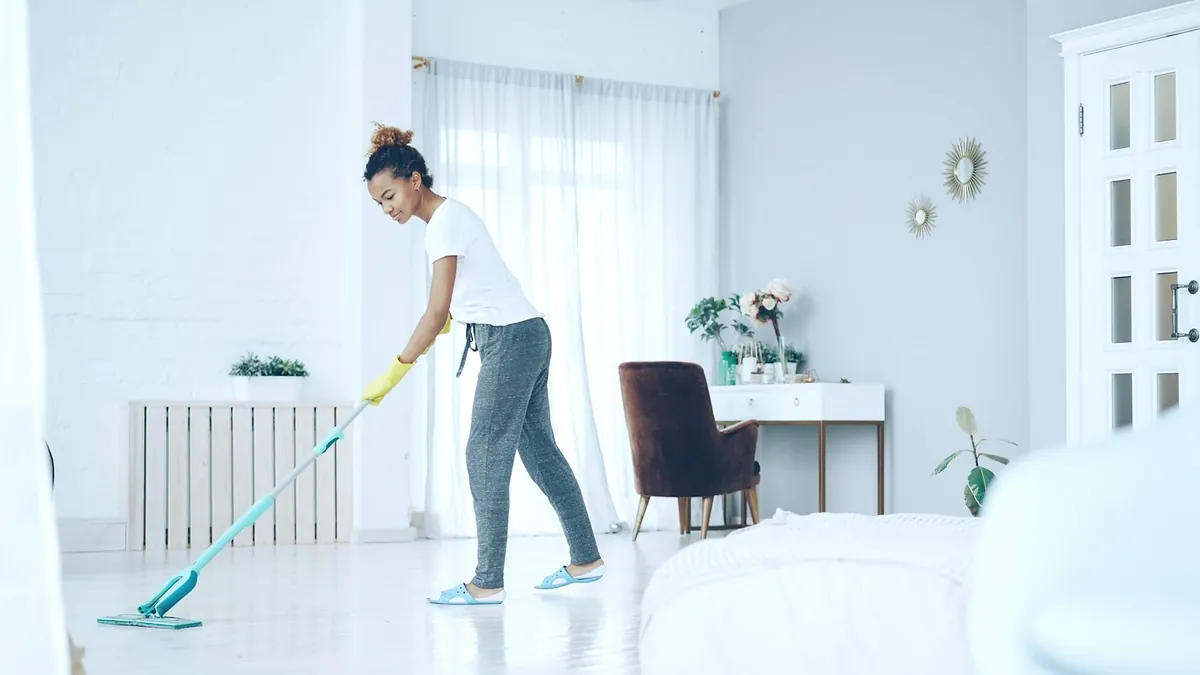 A cleaner in a white T-shirt mopping the white floor of a bright living room