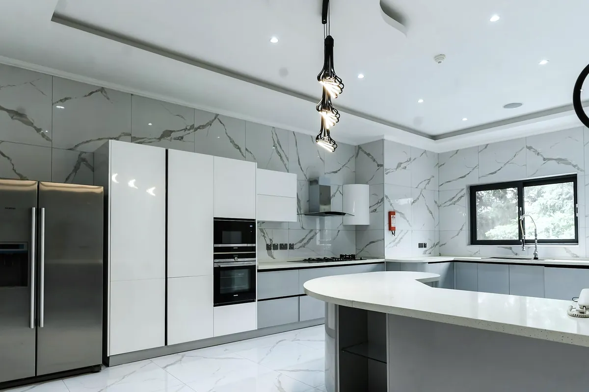 A bright white kitchen with a marble splashback, a steel fridge and a curved island