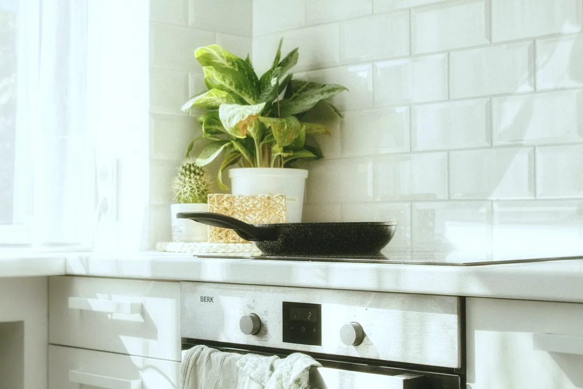 A white kitchen worktop with a potted plant, a frying pan on the hob and a tea towel on the oven door
