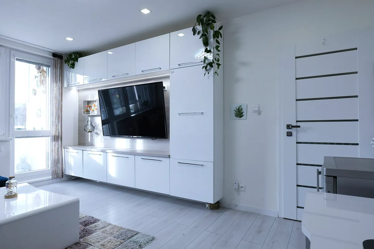 A white living room with a wall of gloss white cupboards around a television