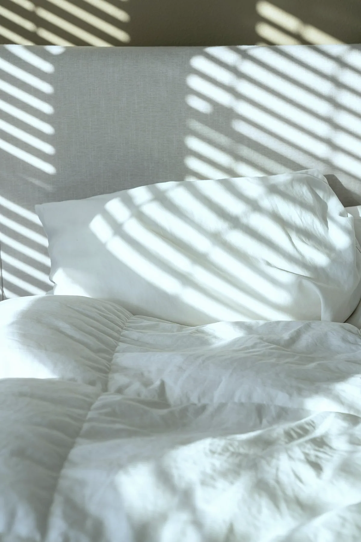 Sunlight falling in stripes across white pillows and a duvet