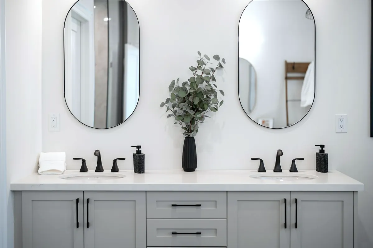 A double basin with two oval mirrors, black taps and a vase of eucalyptus
