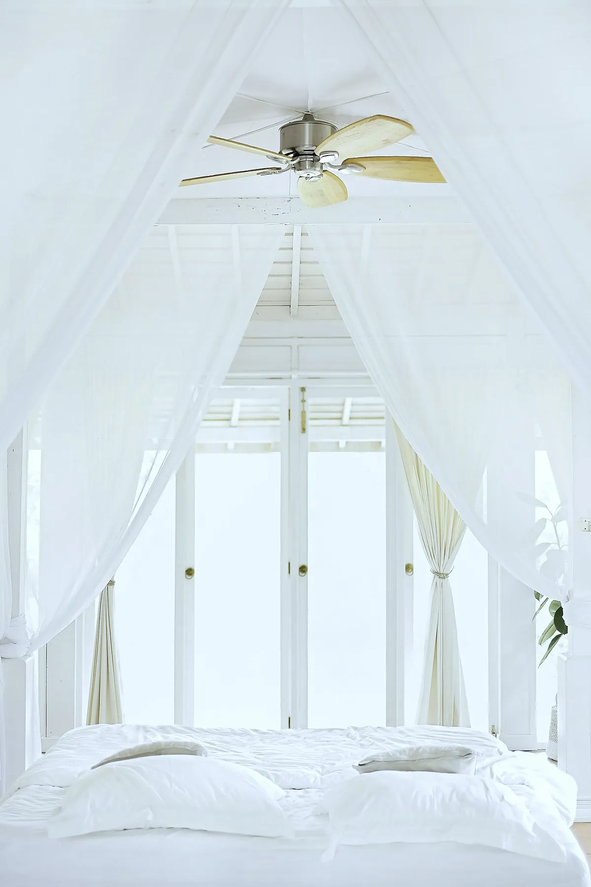 A white four poster bed with sheer curtains in front of tall white doors