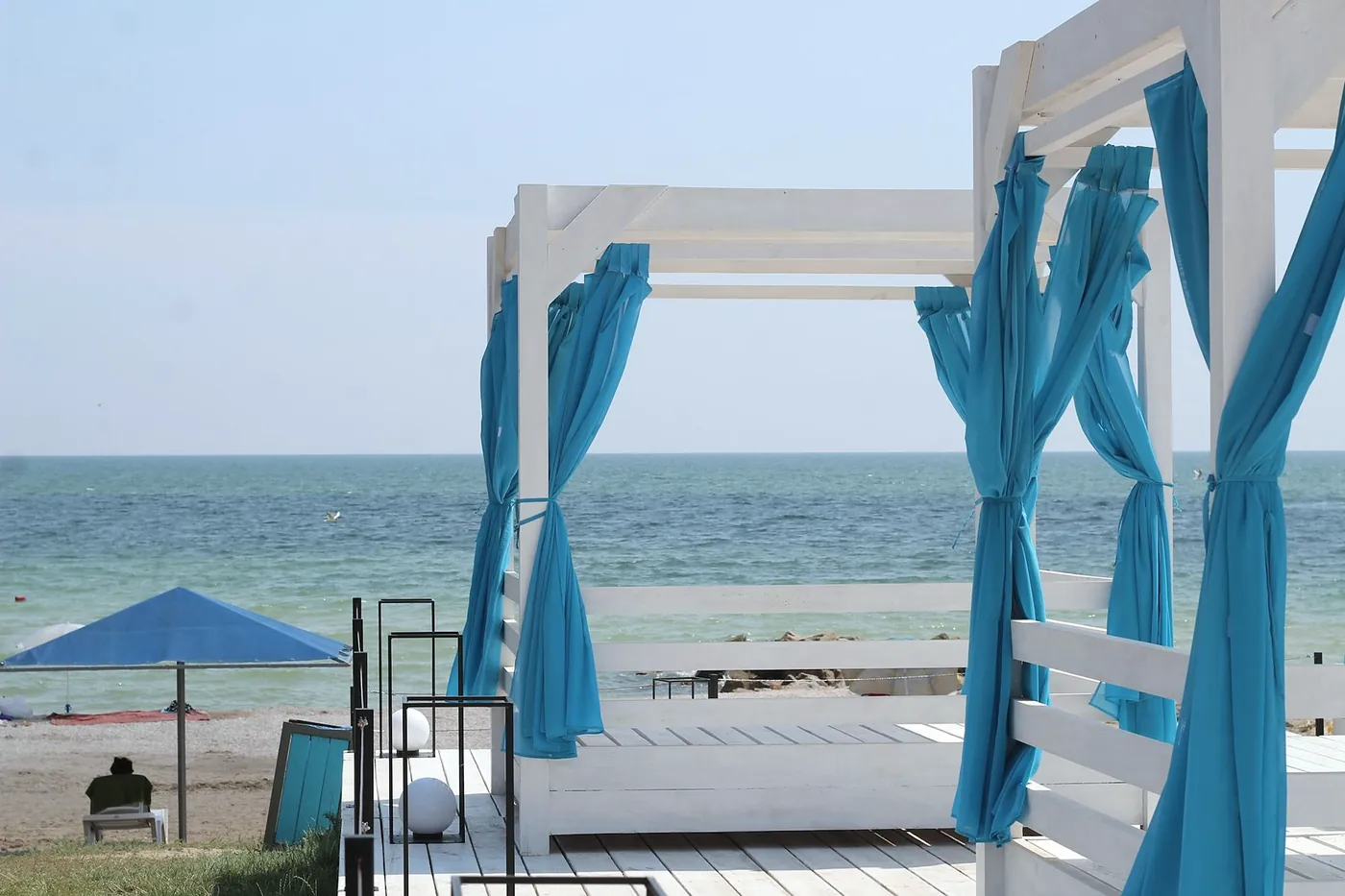 A beach with white cabanas and turquoise curtains, and the sea behind