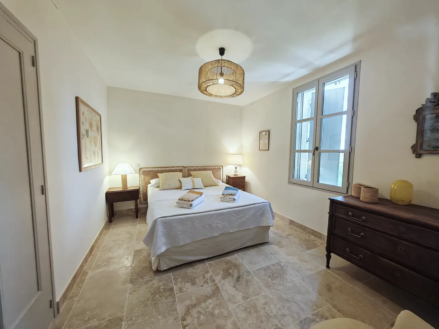 Bedroom with a stone floor, a double bed, bedside lamps and a dark wooden chest of drawers