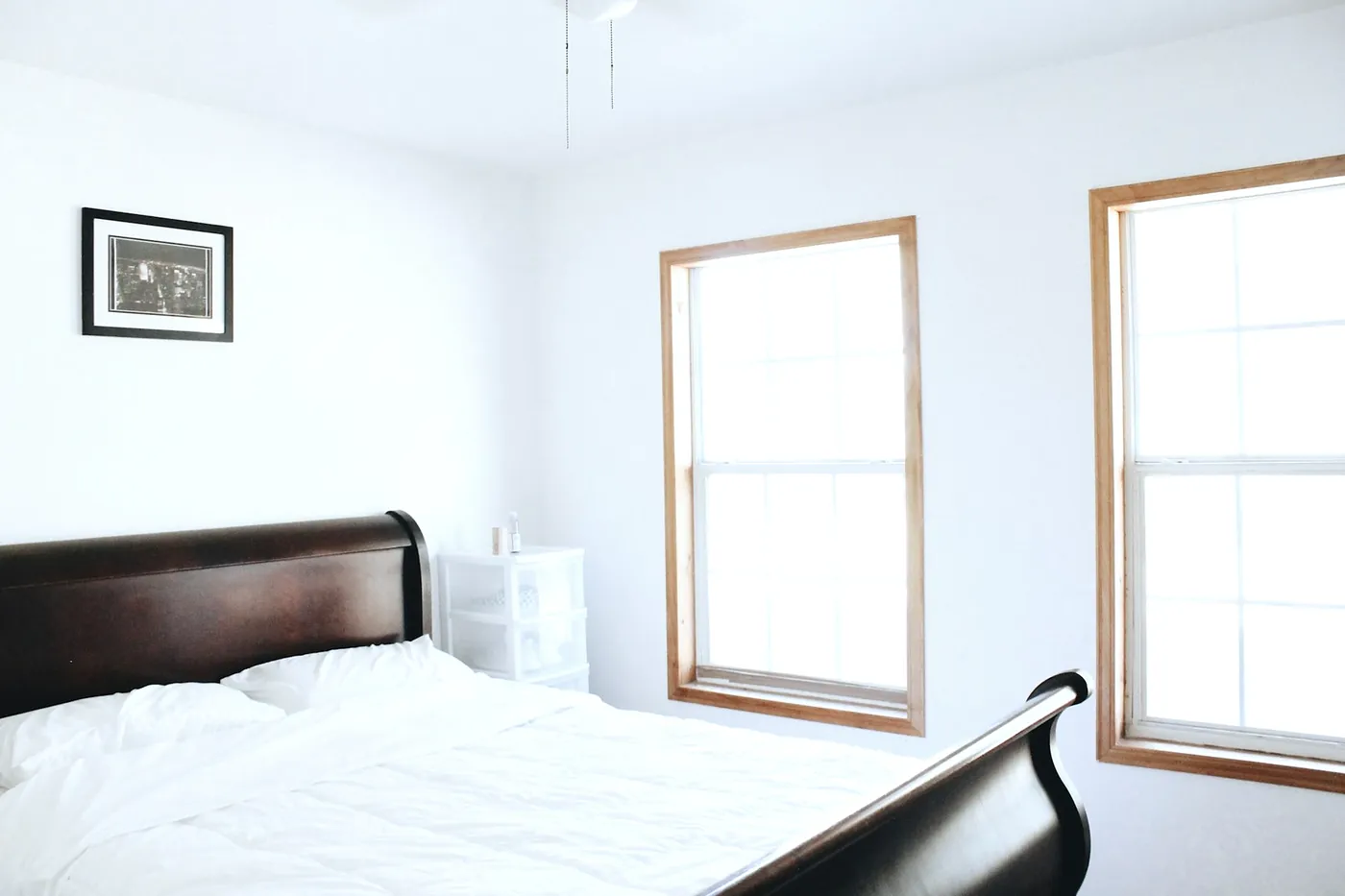 Bright corner bedroom with a dark wooden bed and two tall windows with wooden frames