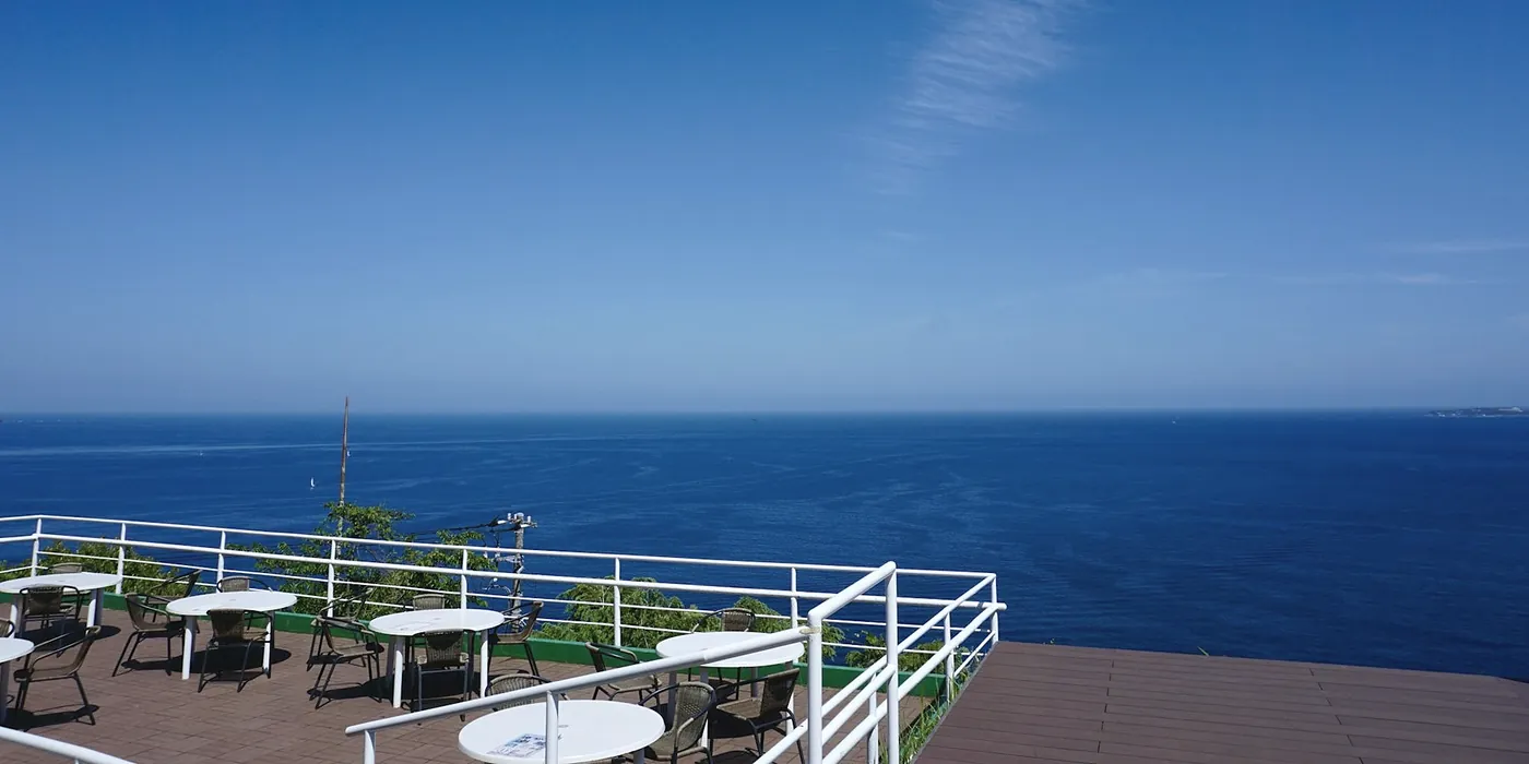 Tables and chairs on the roof terrace above a wide, deep blue sea