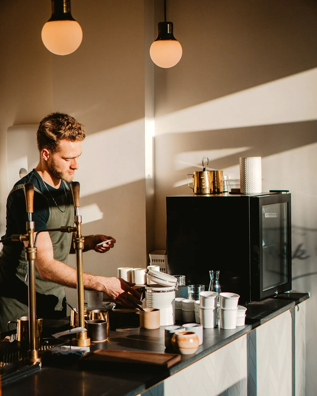 A barista working at the espresso machine with morning sun coming through the window