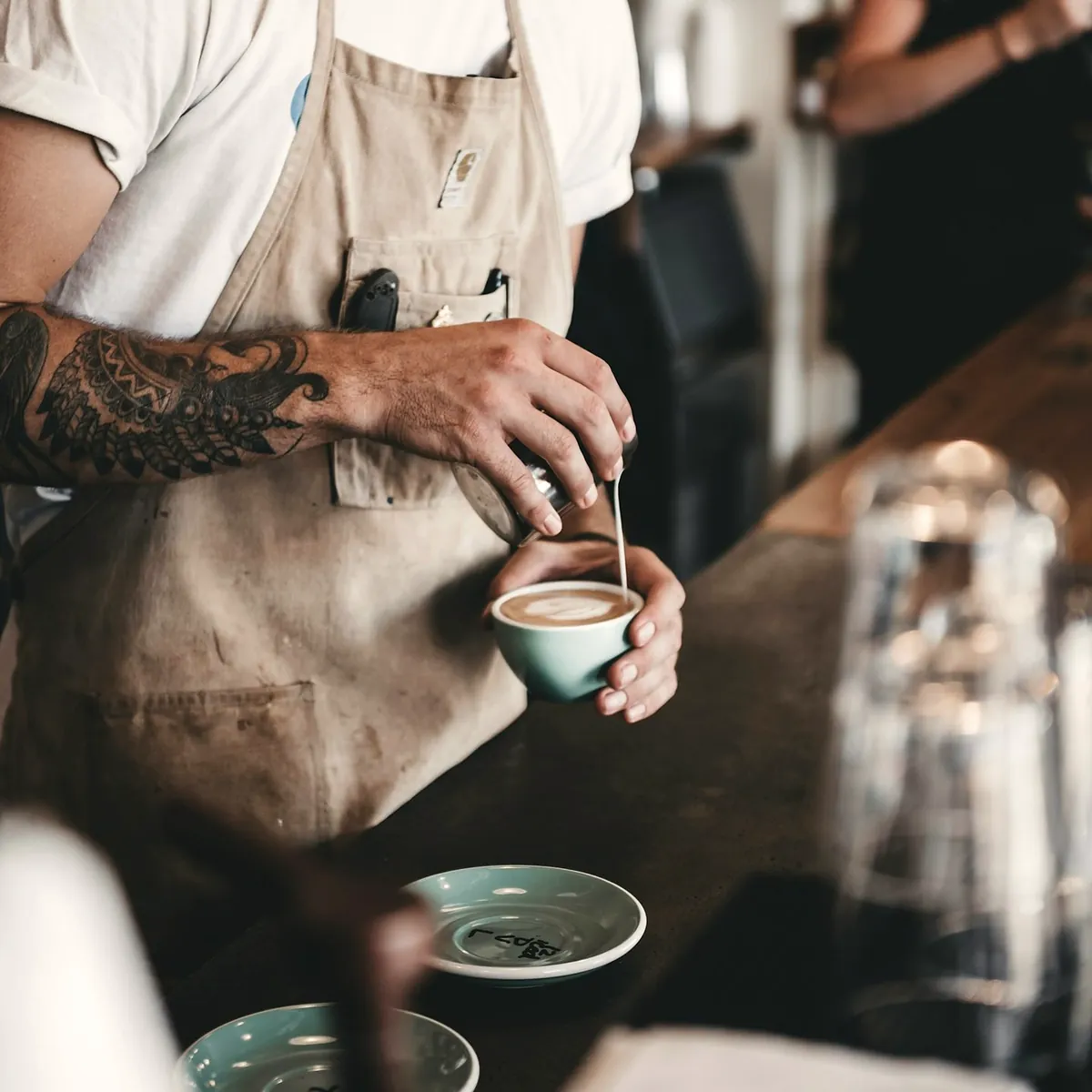 A barista in an apron pouring milk into a cup at the bar