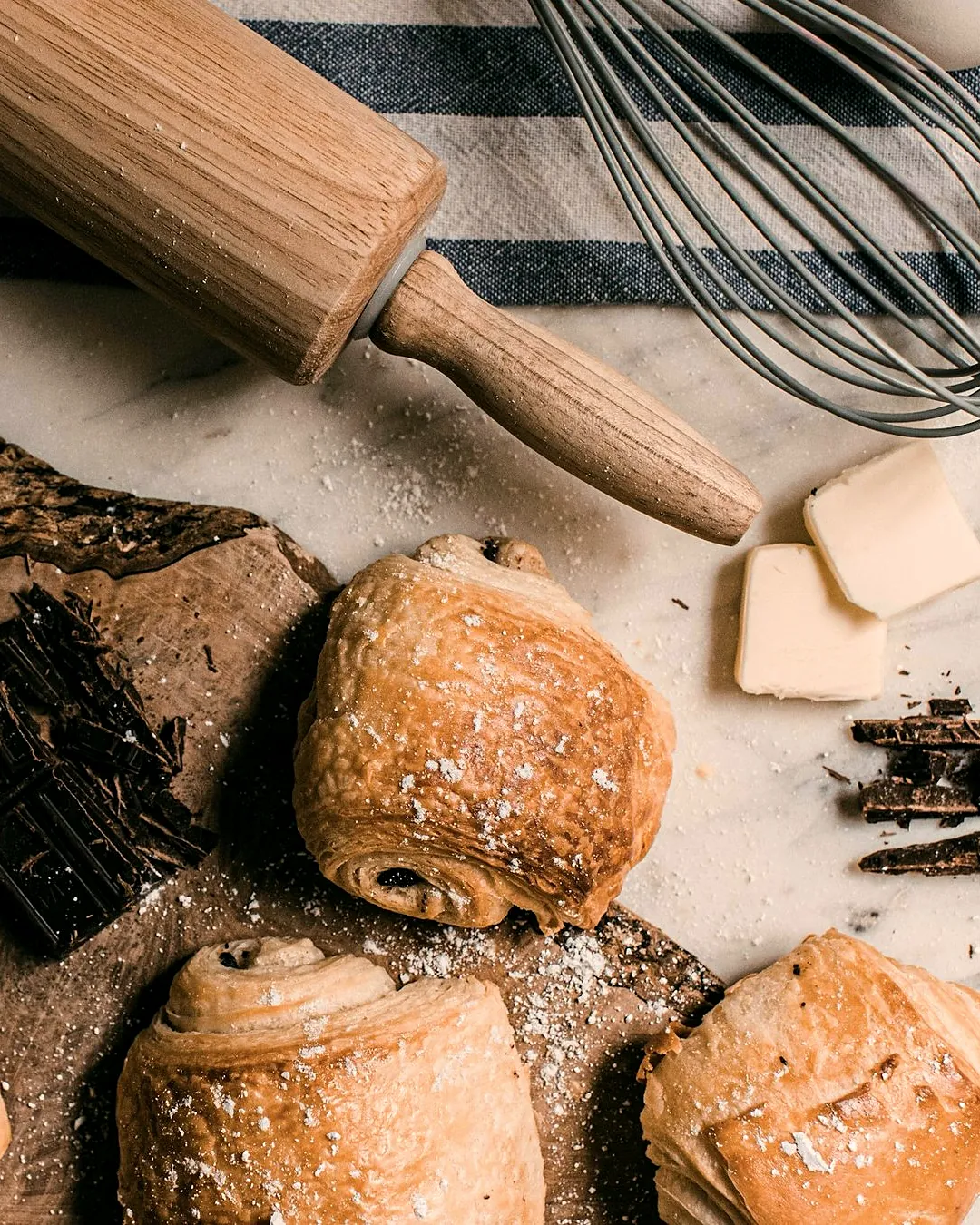 Pains au chocolat on the bakery bench, with a rolling pin, butter and chopped chocolate