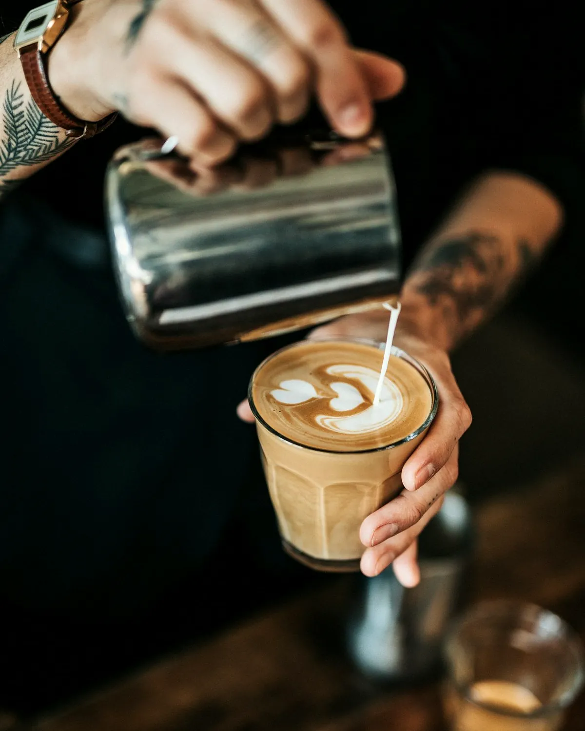 Steamed milk being poured into a glass of espresso to make a cortado
