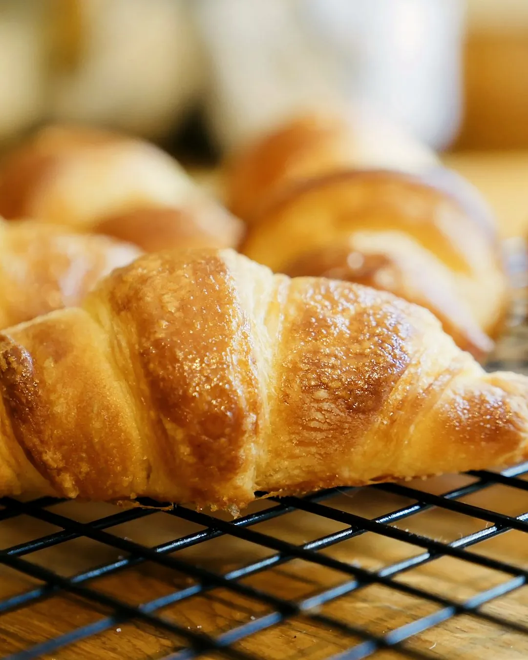 A butter croissant cooling on a wire rack, more croissants behind it