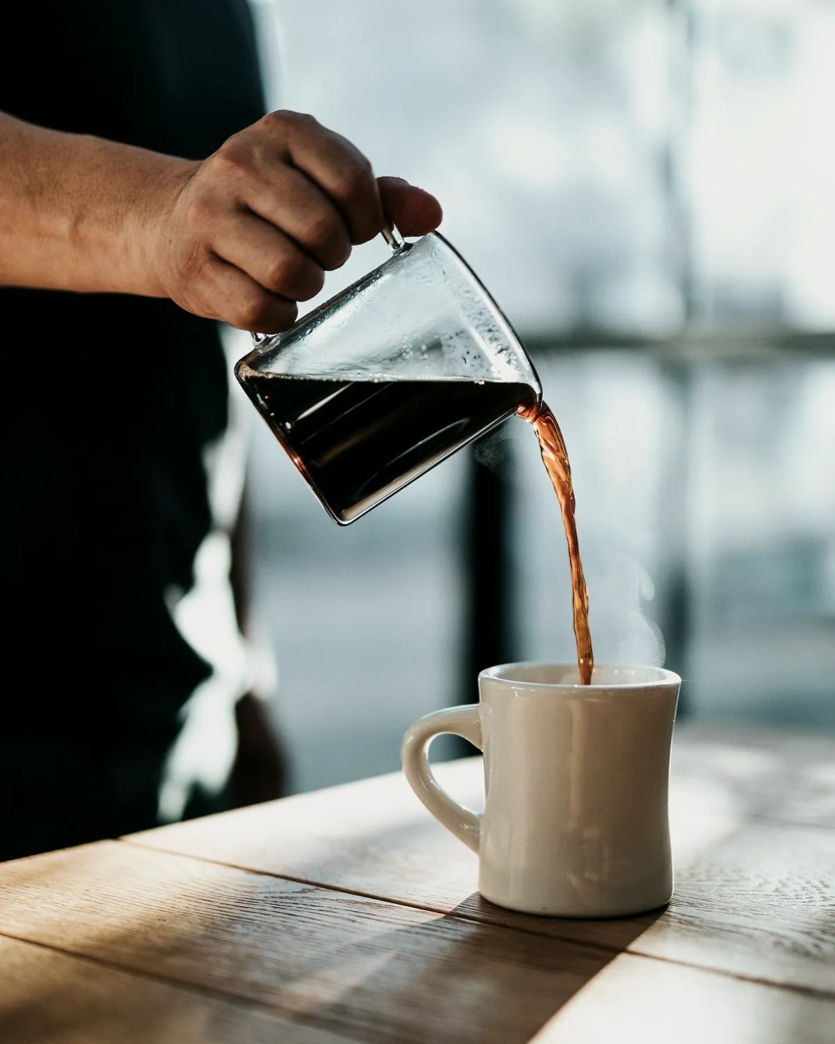 Filter coffee being poured from a glass jug into a white mug
