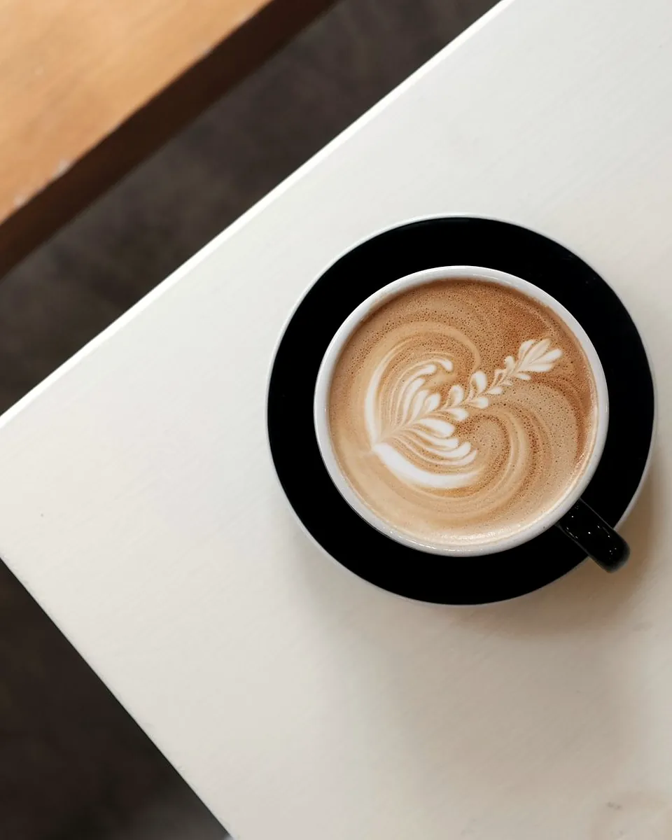A flat white in a black cup on a white table, seen from above