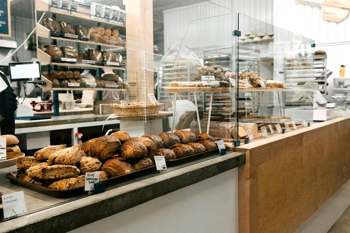 The bakery counter at lunchtime, with a tray of scones and croissants in front and loaves on the shelves behind