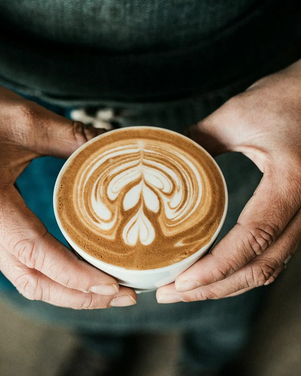 Two hands holding a latte with a tulip drawn in the foam