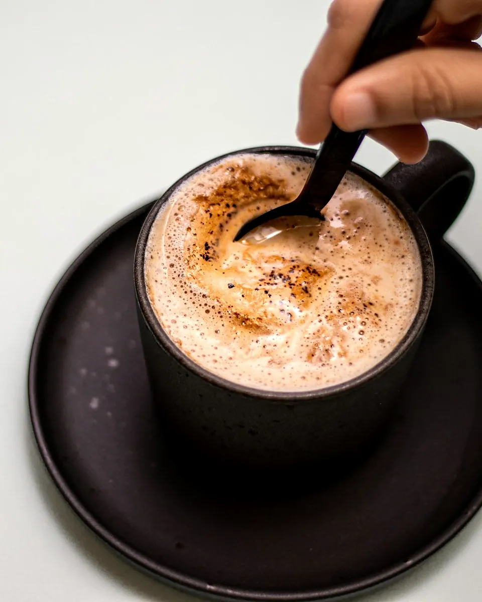 A mocha with cocoa on the foam being stirred with a spoon