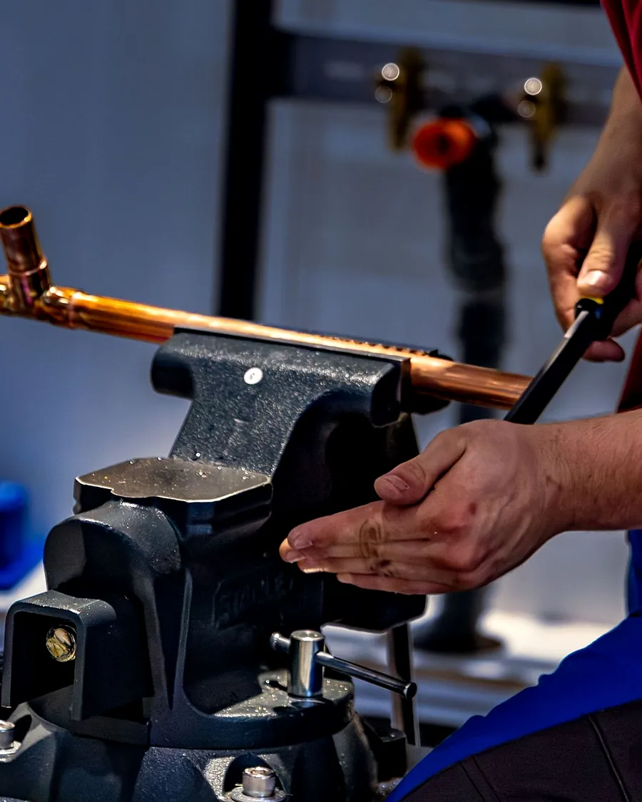 A plumber holding a length of copper pipe in a bench vice