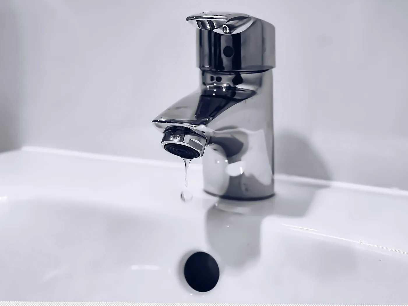 A chrome basin tap with a drop of water hanging from the spout