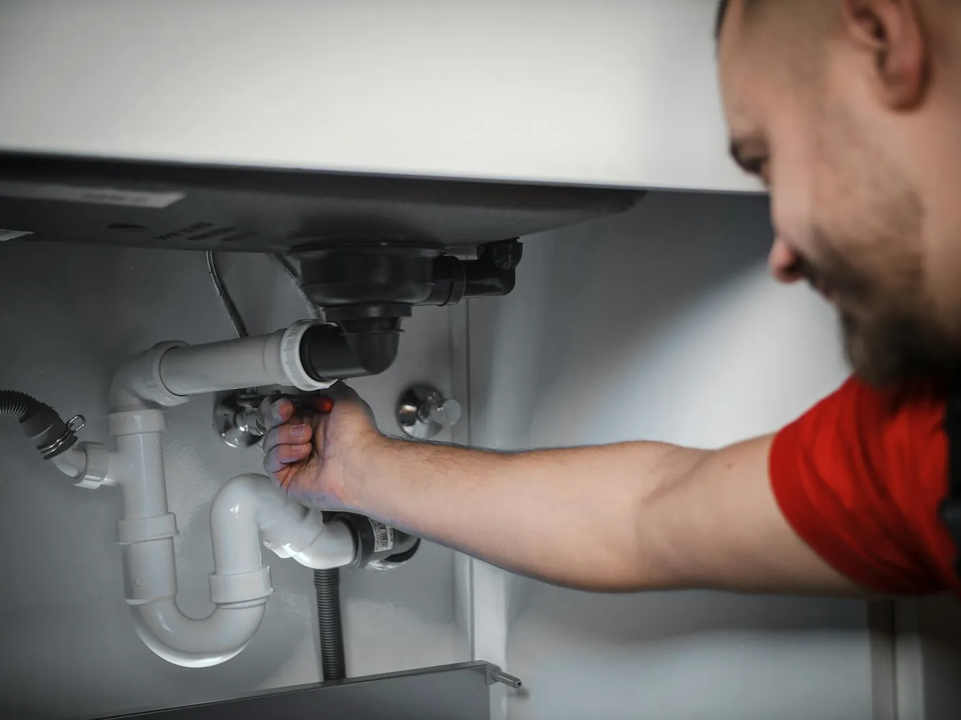 A smiling plumber reaching under a sink to undo a waste pipe