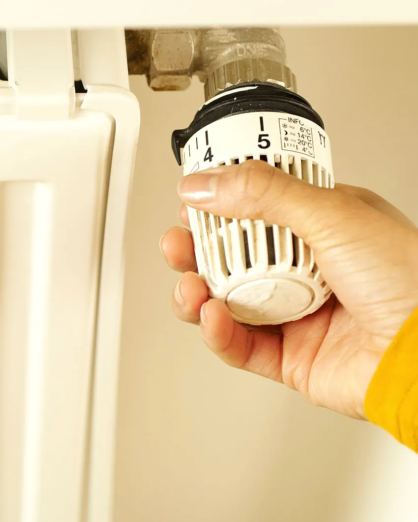 A hand turning the thermostatic valve on a white radiator