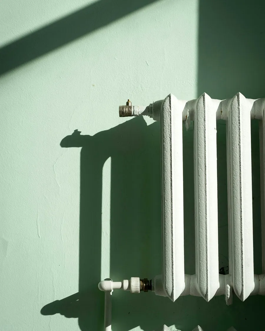 An old white column radiator on a pale green wall in afternoon sun