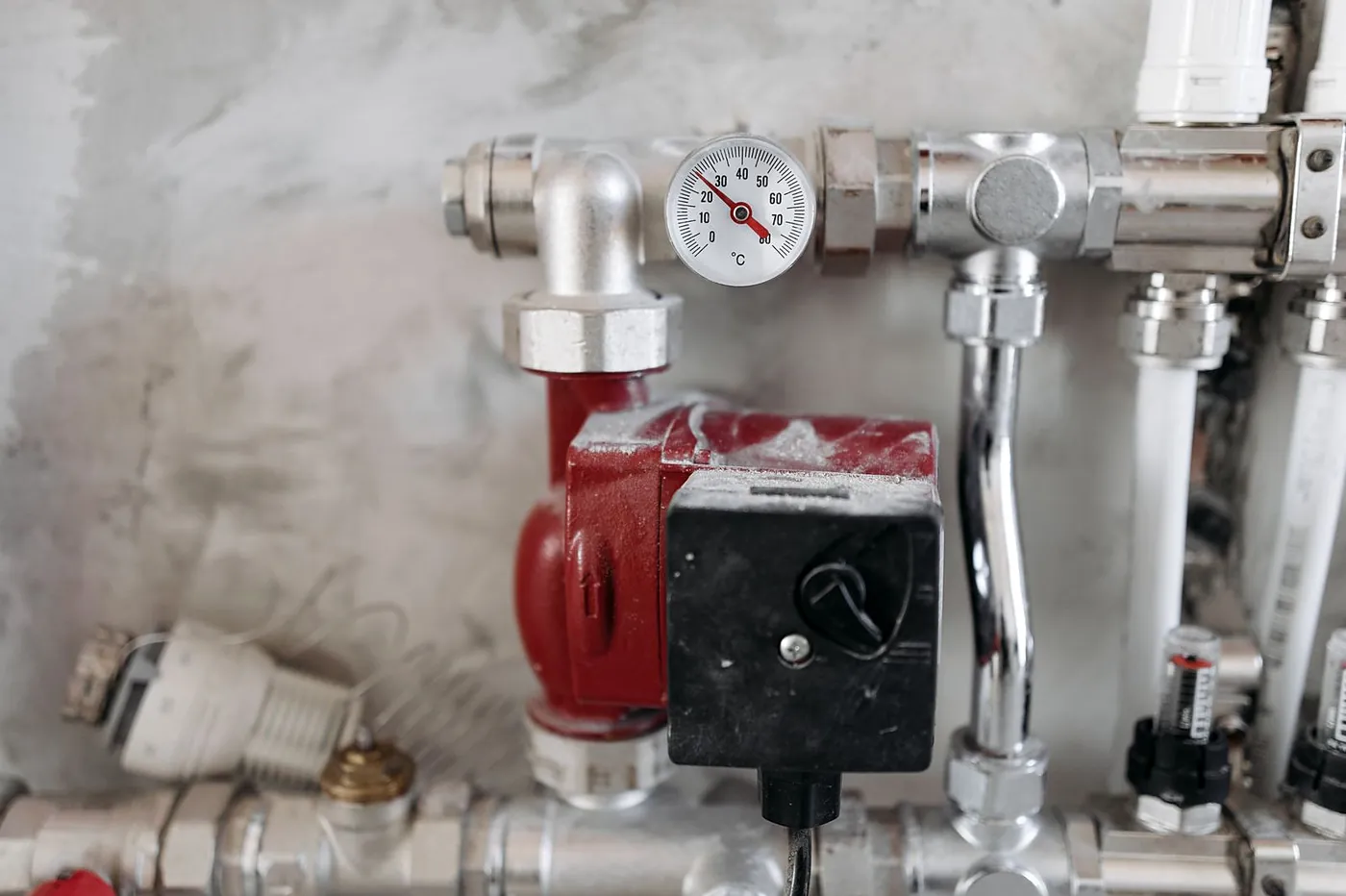 A heating manifold with a red pump, a temperature gauge and chrome pipework
