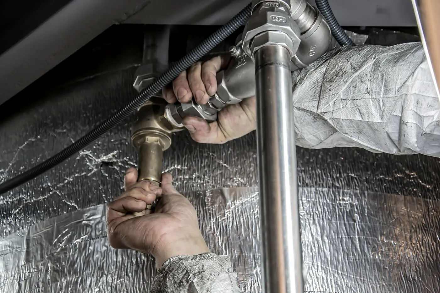 Two hands tightening a joint on a steel pipe in a foil lined ceiling space