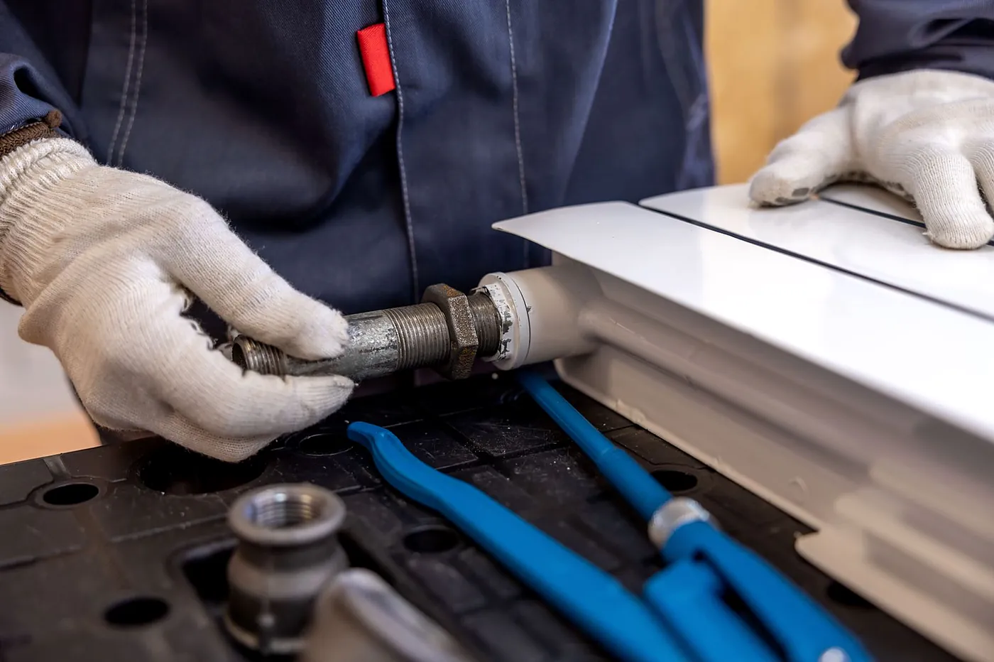 Gloved hands fitting a valve to the end of a new white radiator