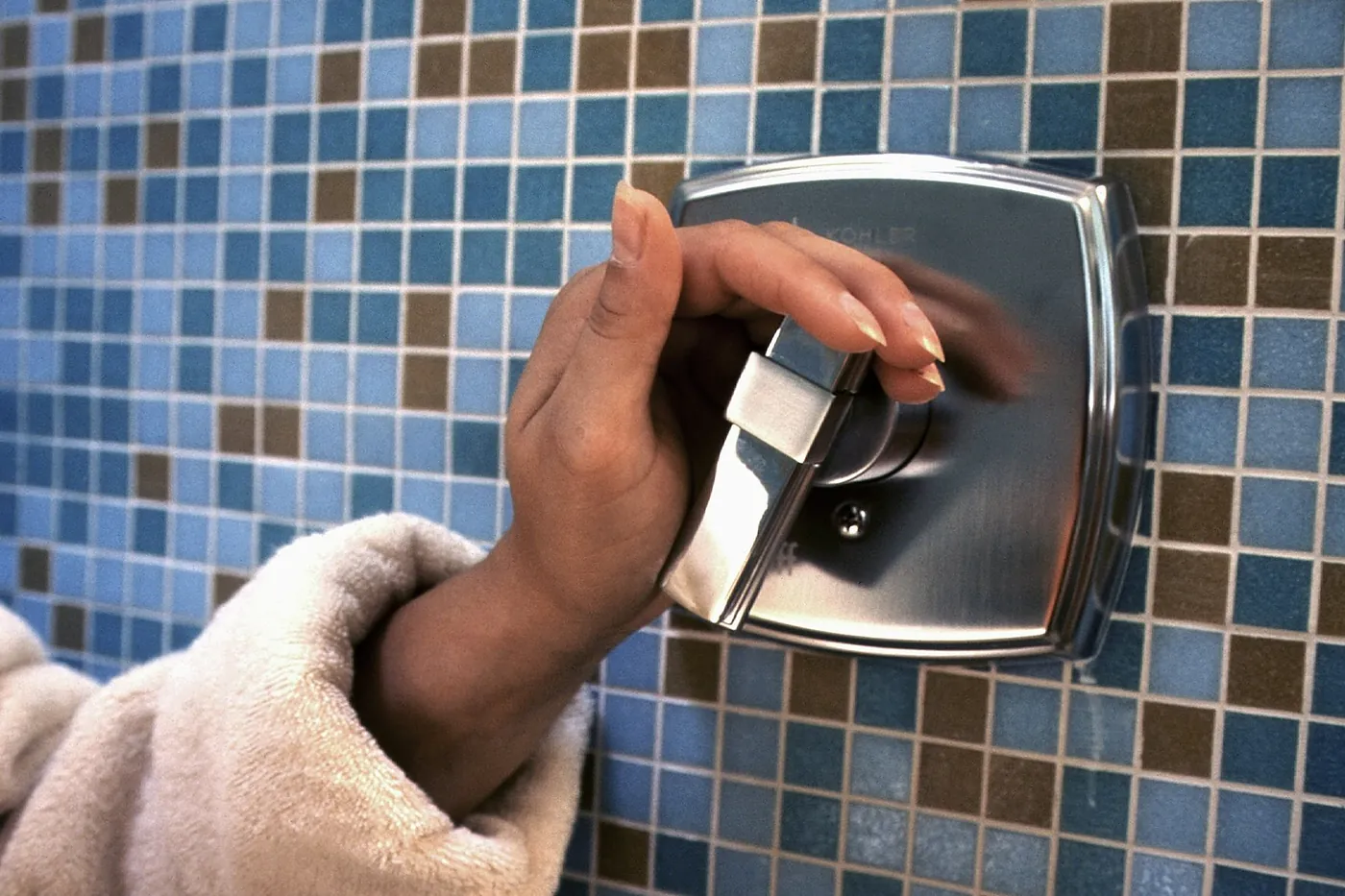 A hand turning a square chrome shower mixer on a blue tiled wall