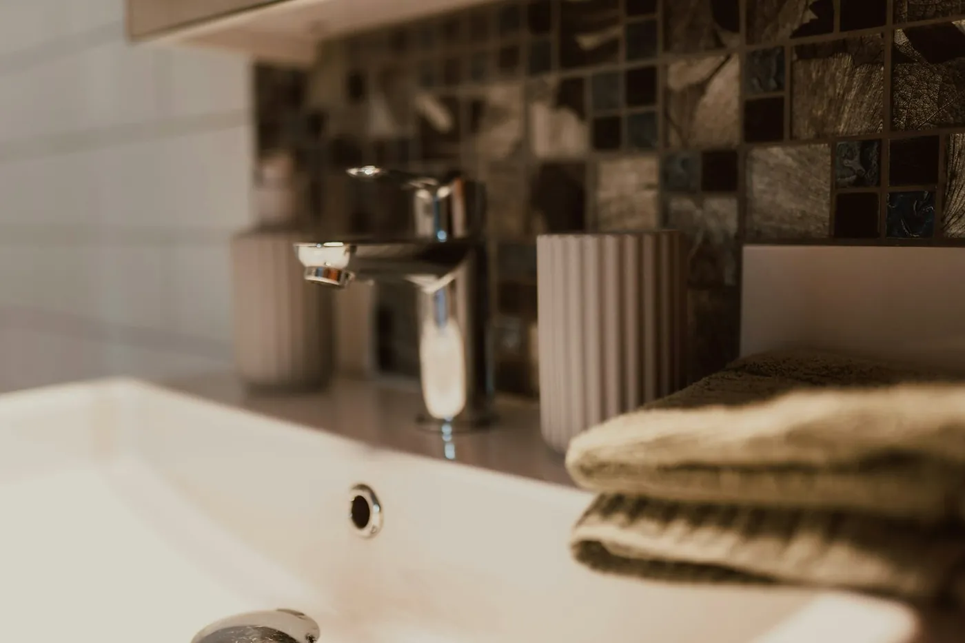 A chrome basin tap beside folded towels in a tiled bathroom