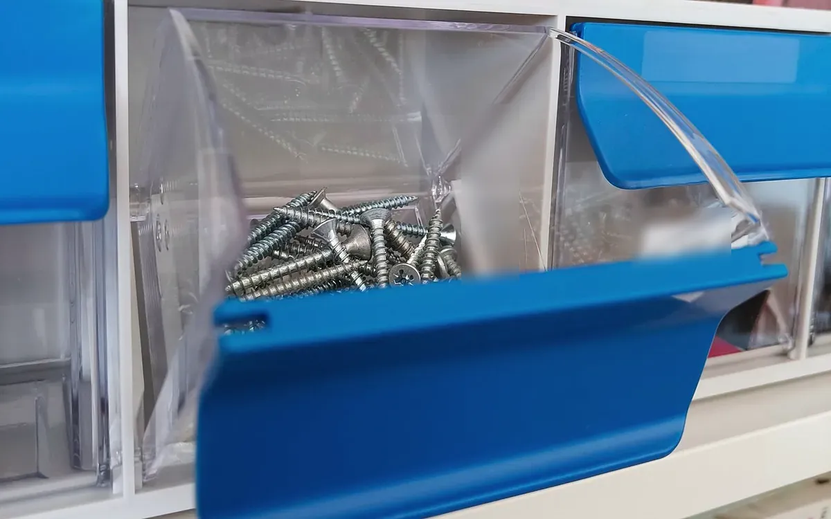 A blue bin of loose countersunk screws on a wall of storage bins
