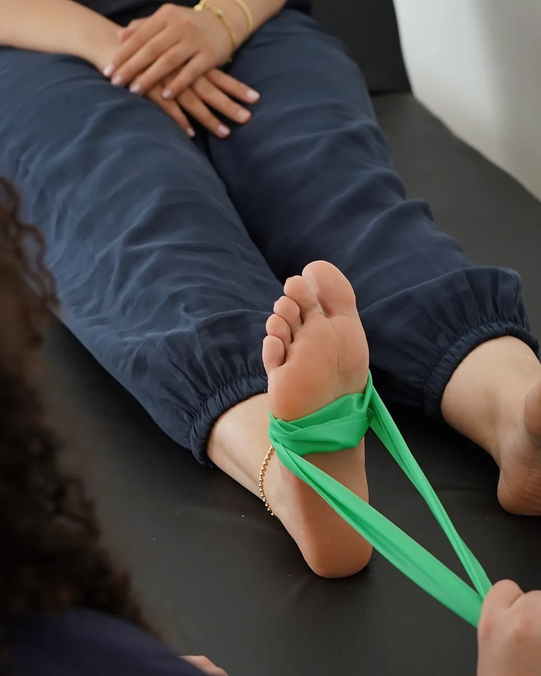A patient's foot looped in a green resistance band on a treatment table
