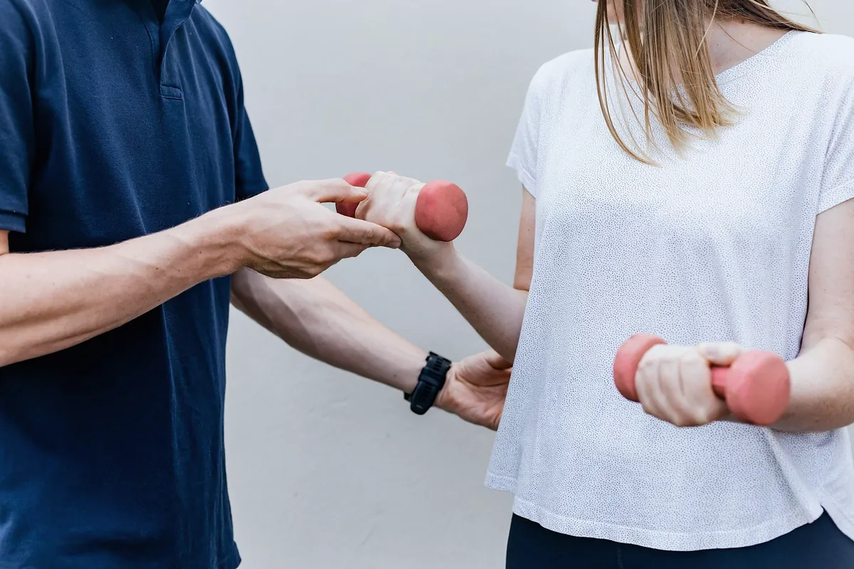 A physiotherapist supporting a woman's elbow as she lifts a small pink dumbbell