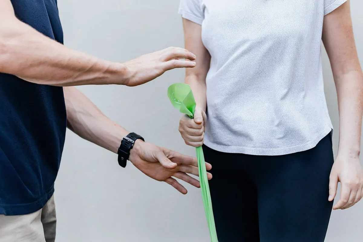 A physiotherapist showing a woman how to hold a green exercise band at her side