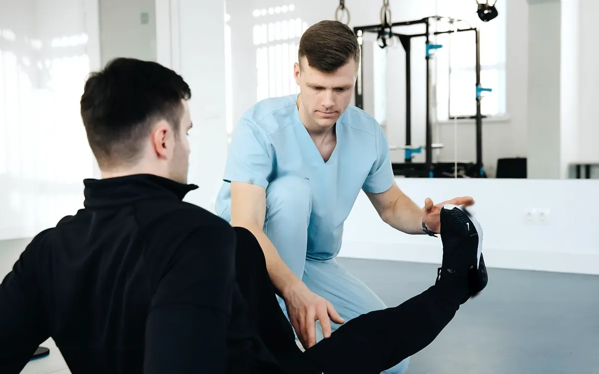 A physiotherapist kneeling beside a seated man and supporting his raised foot