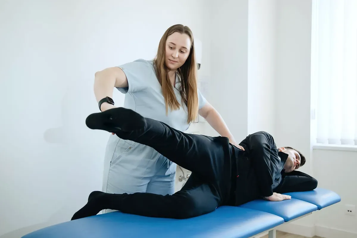 A physiotherapist lifting the top leg of a man lying on his side on a blue treatment table