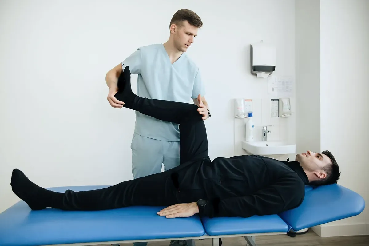 A physiotherapist lifting the bent leg of a man lying on his back on a blue treatment table