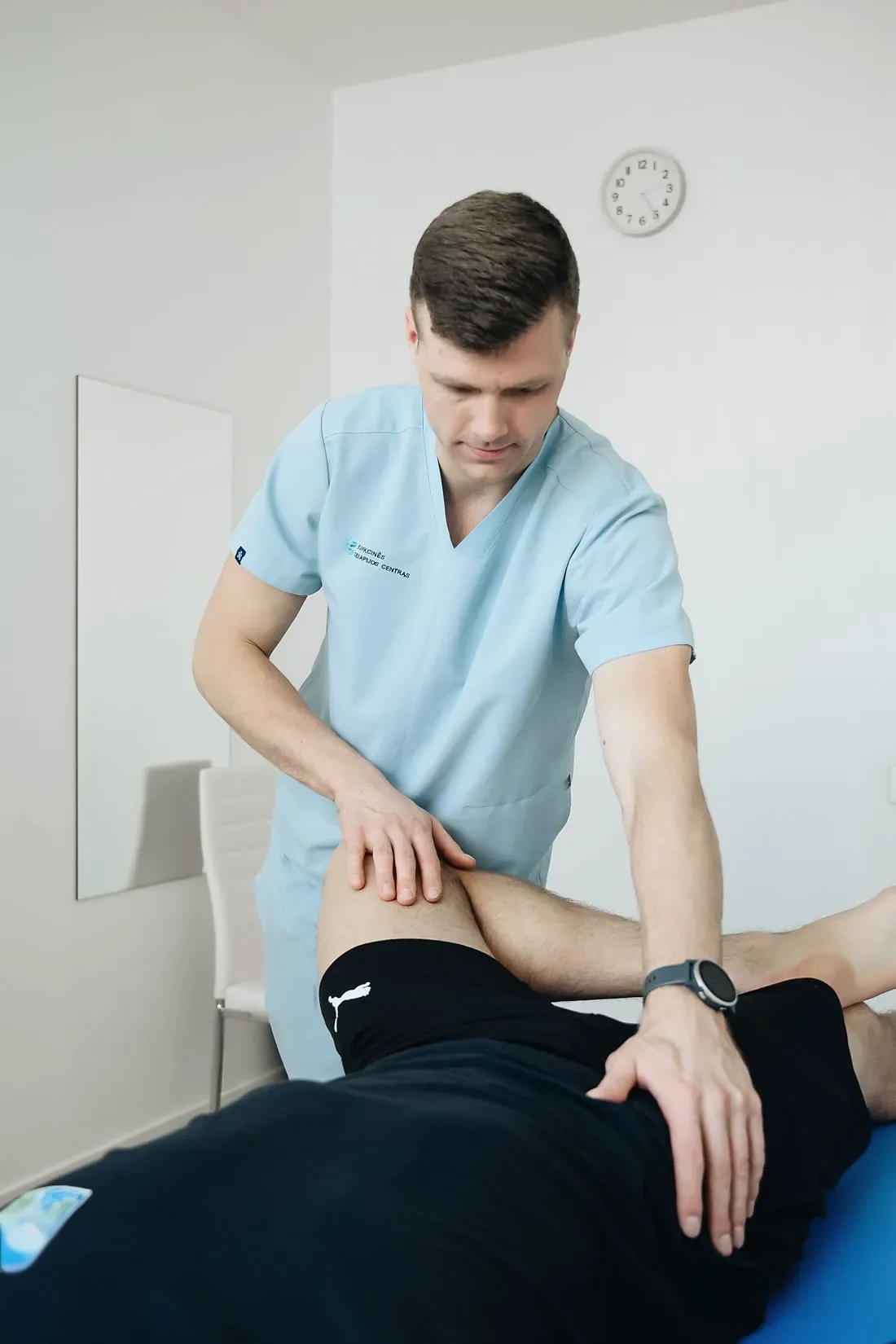 A physiotherapist in light blue scrubs working on the thigh of a patient lying on a table