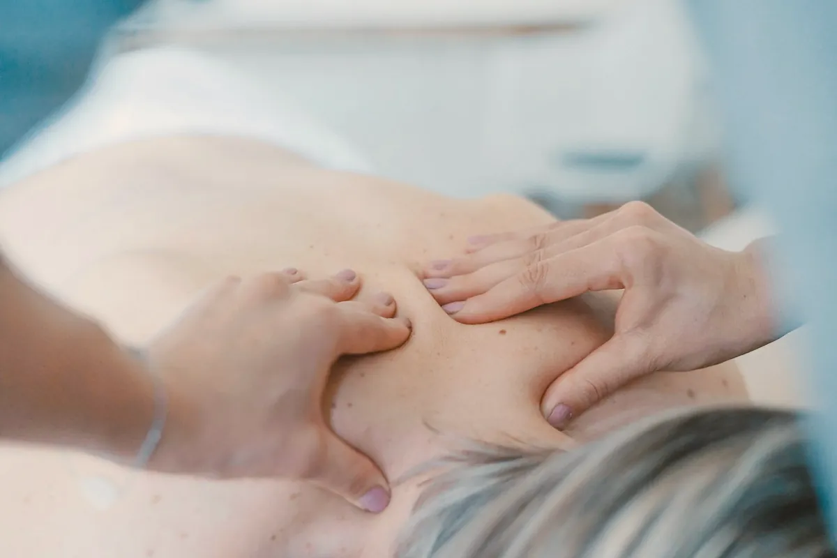 A physiotherapist's hands working on the muscles between a woman's neck and shoulder blade