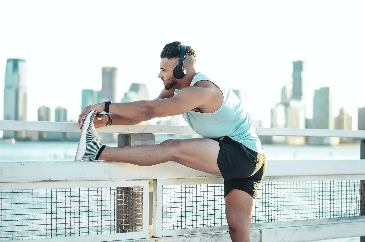 A runner stretching his hamstring with one leg on a railing by the water