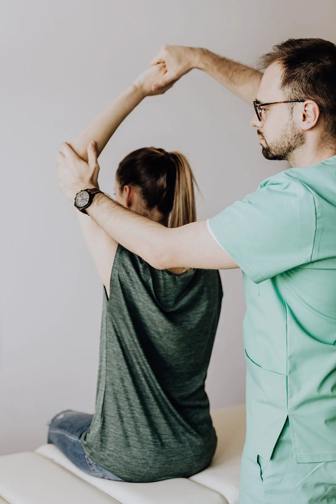 A physiotherapist guiding a seated woman's arm up over her head