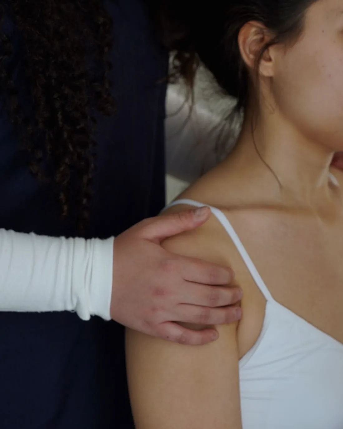 A practitioner's hand resting on a woman's shoulder to feel how it moves