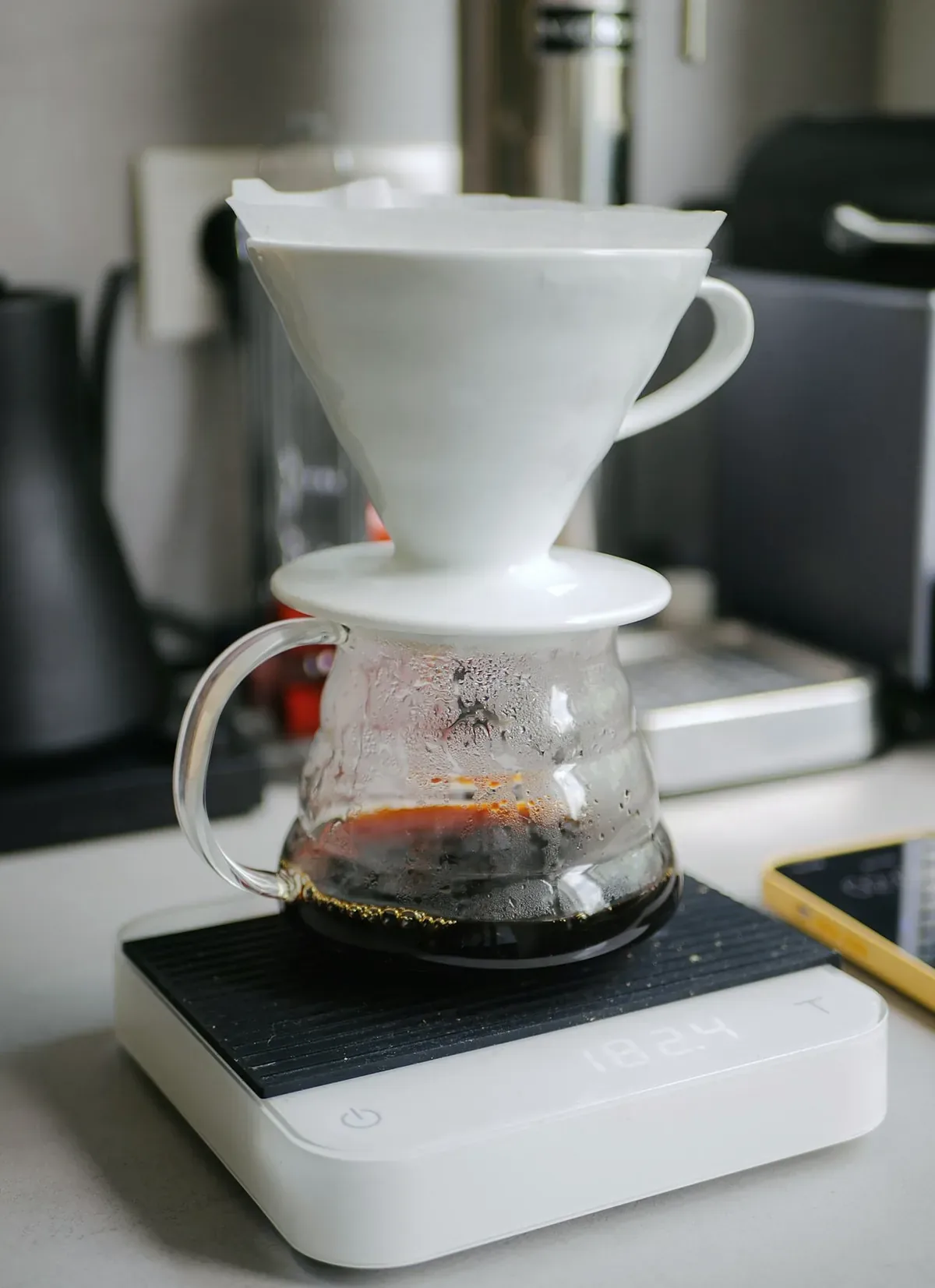 A white ceramic cone brewer on a glass server, standing on a brew scale