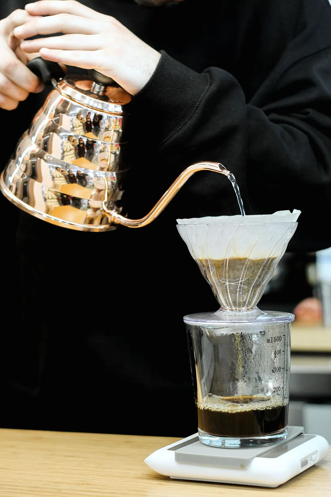 A copper coloured gooseneck kettle pouring a thin stream into a pour over brewer