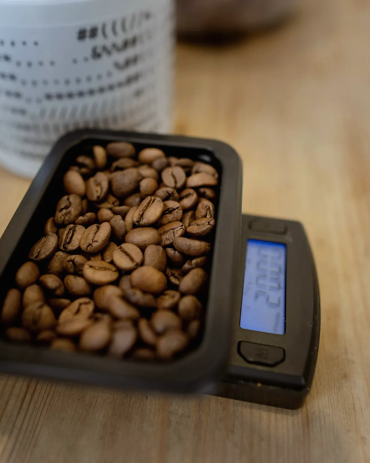 A tray of roasted coffee beans on a small digital scale on a wooden table