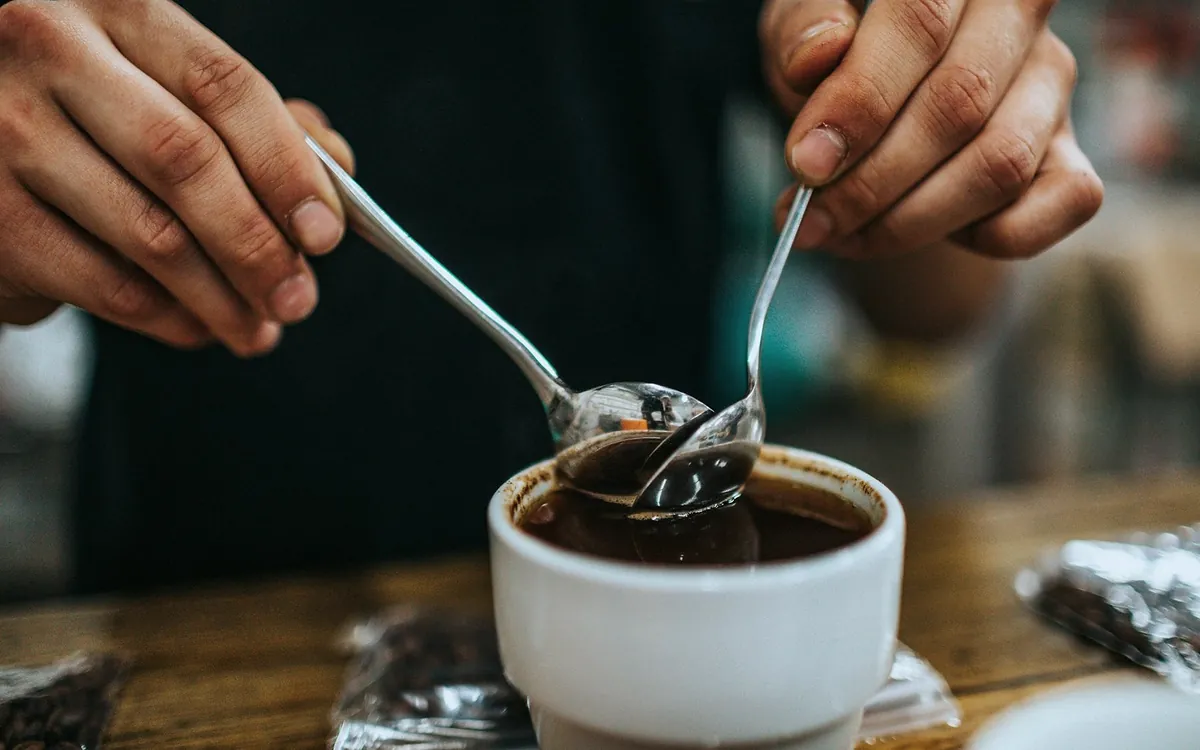 Two cupping spoons skimming the crust from a white cupping bowl