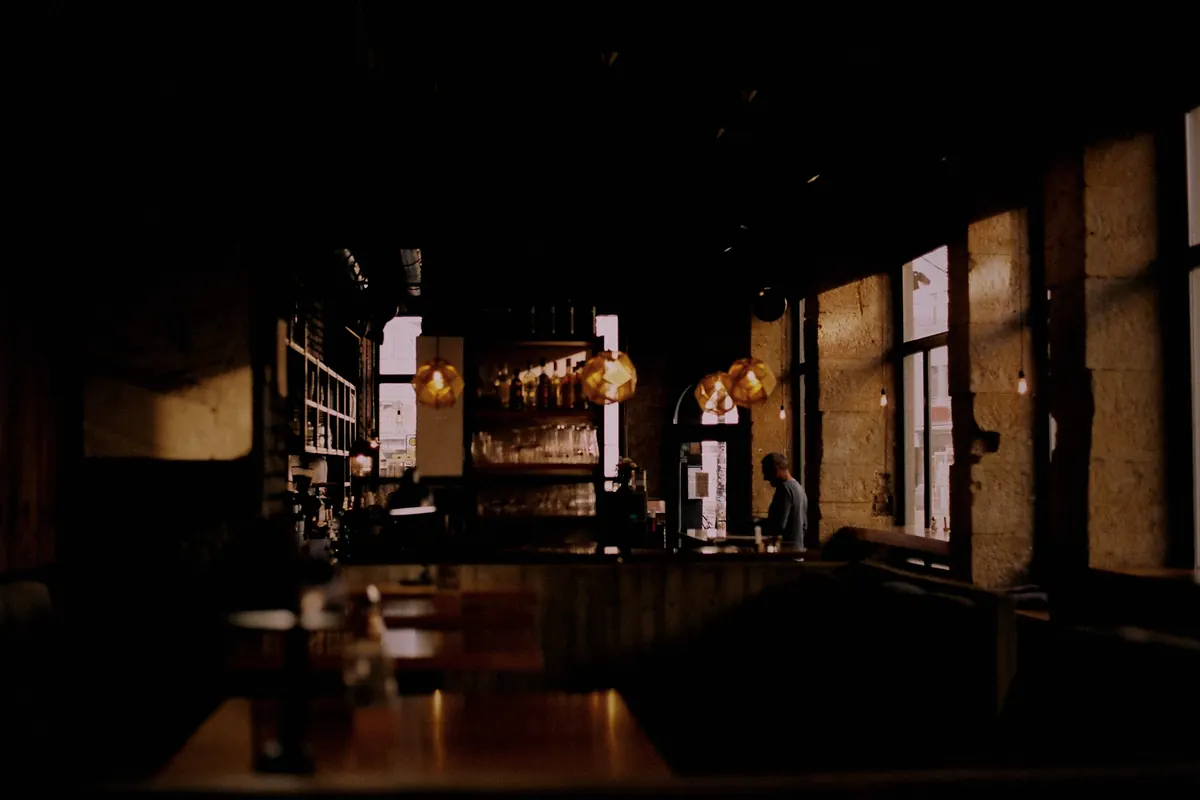 The bar at night, with bottles lit on the back wall and windows along one side