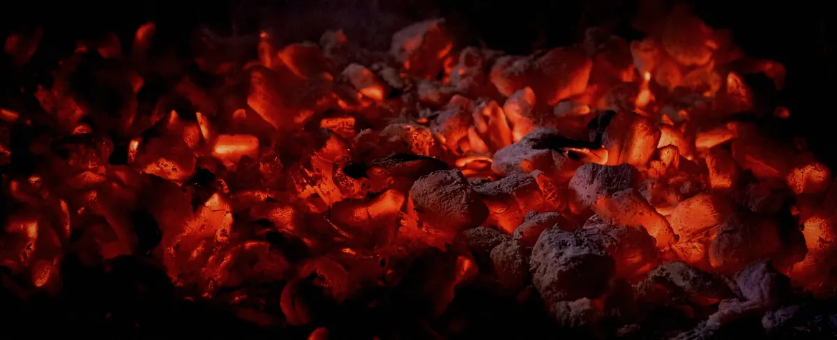 A wide bed of glowing red embers under grey ash